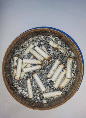 Kötü bağımlılık. Kül tablası ve sigaralar yakın plan. Masadaki kül tablasının yakın görüntüsü. Bir sürü yanmış sigara izmariti ve biraz da kül. Kül tablasında yanan sigaranın tepesinde.