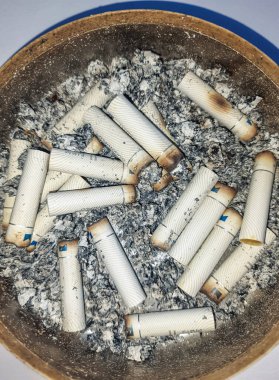 Kötü bağımlılık. Kül tablası ve sigaralar yakın plan. Masadaki kül tablasının yakın görüntüsü. Bir sürü yanmış sigara izmariti ve biraz da kül. Kül tablasında yanan sigaranın tepesinde.