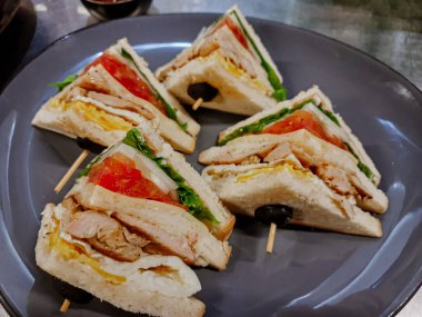 Jambonlu sandviç, peynir, domates, marul, tavuk eti ve kızarmış ekmek. Sandviç masada..