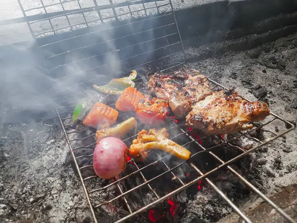 stock image Delicious grilled meat on a barbecue grill with smoke and flames. Barbecue skewers meat kebabs with vegetables on a flaming grill.