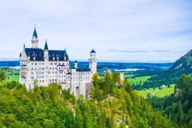Neuschwanstein, ünlü masal kalesi, prensesler ve sevgililer, mavi gökyüzüne ve ormanlara karşı durur göllerin arka planına karşı