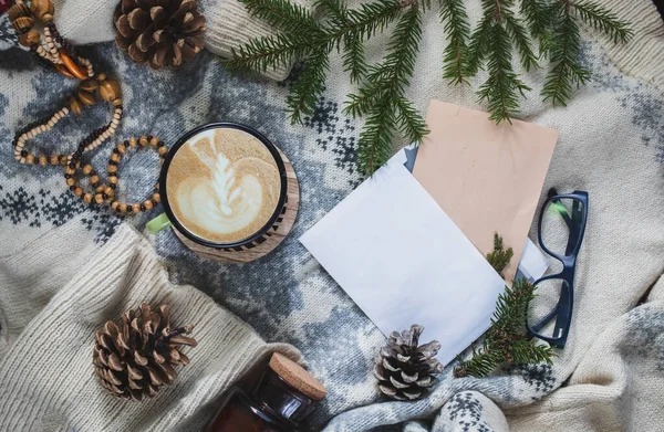 Winter cozy background with a cup of coffee, a warm sweater, spruce branch, glasses and blank letter. Flat lay for bloggers. Winter season template for feminine blog social media.