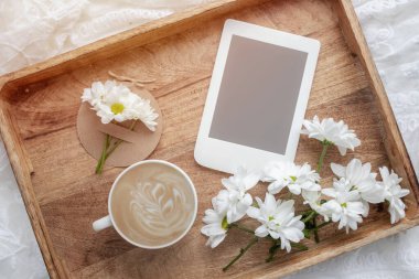 Romantik kompozisyon, bir fincan kahve, beyaz çiçekler ve ahşap tepside fotokopi alanı olan e-okuyucu. Kadınsı blog sosyal medya şablonu.
