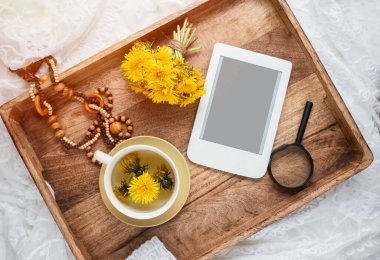 Tahta tepside bir fincan sağlıklı karahindiba çayı ve e-kitap. Bitkisel ilaçlar. Düz stil. Kadınsı blog sosyal medya şablonu. 