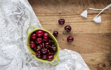 Küçük bir kasede tatlı kirazlar ve ahşap masanın etrafına saçılmış. 