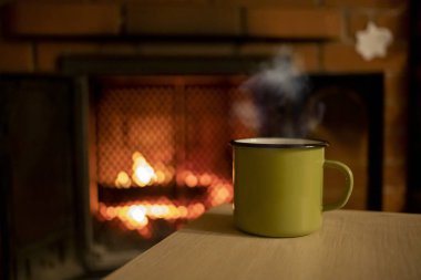 A mug with hot tea in front of a burning fireplace