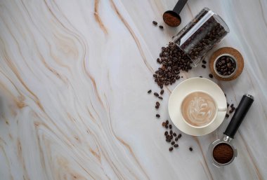 Bir fincan kapuçino, cam kavanozda kahve çekirdekleri ve arka planda hafif mermer masa tozuyla kompozisyon. Kahve konsepti. Kahve arka planı.