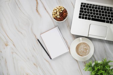 Laptop kalem, kağıt defter, bitki, kahve fincanı ve fındık karışımı beyaz mermer masa arkaplanındaki fındıklı iş yeri fotoğrafı..
