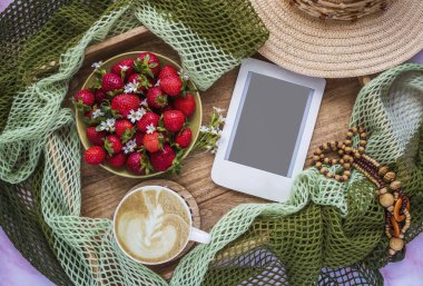 Bir fincan kahveyle romantik kompozisyon, bir tabak sulu çilek ve ahşap tepside fotokopi alanı olan e-okuyucu. Kadınsı blog sosyal medya şablonu.