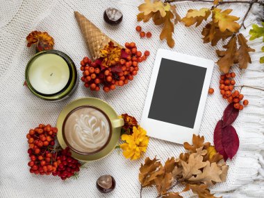 Sonbahar evi kompozisyonu, bir fincan kahve, fotokopi alanı olan e-kitap, sonbahar yaprakları ve beyaz örülmüş arka planda rowan dalları. Feminen blog sosyal medya için sonbahar şablonu.