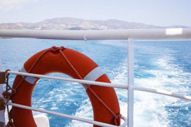 Mavi denizin arka planındaki gemide kırmızı can simidi. Turuncu renkli can yeleği beyaz bir tırabzanda asılı Yolcu gemisinde.