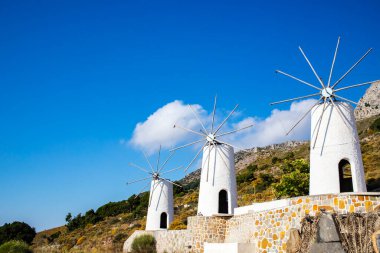 Yeşil tepe ve mavi gökyüzü arka planında üç eski Akdeniz yel değirmeni.