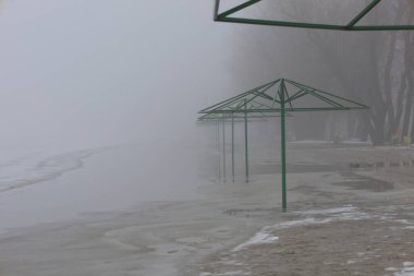 Beach umbrellas on the winter beach, Chernihiv city, fog in the city clipart