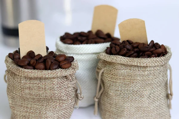 Coffee beans in burlap bags with blank labels on white background. Close-up image with coffee beans.
