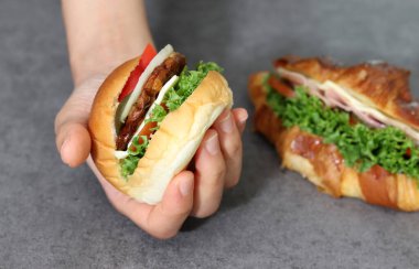 Hamburger tutan bir elin görüntüsünü yaklaştır. Sebzeli ekmek ve etli börek..