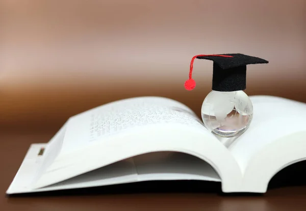 A transparent globe with a bachelor\'s cap on an open book. Global business learning.