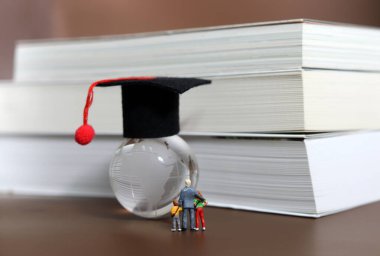 Küresel erken eğitime ilgi kavramı. Mezuniyet şapkalı bir küreye bakan minyatür insanlar..