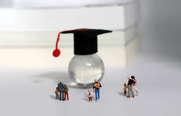 The concept of interest in global early education. Miniature people looking at a globe with graduation caps on it.