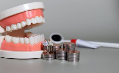 Yaşlılar için diş masraflarının yükü. Yaşlı bir adam ve diş modelinin önünde bir yığın bozuk para..