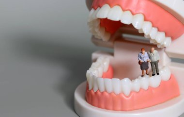 Yaşlı minyatür insanlar diş modelleri üzerinde yürüyorlar. Yaşlılar için diş sağlığı konsepti.
