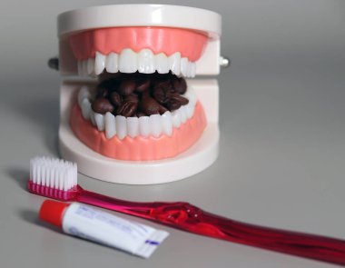 Ağzını dolduran kahve çekirdekleri ve diş bakımı aletleri. Diş sağlığı bozuk içecek konsepti.