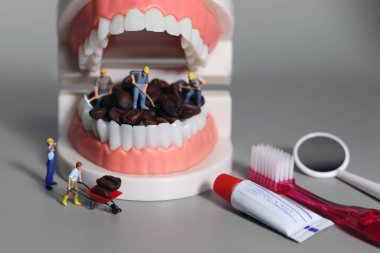 Minyatür insanlar kahve çekirdeklerini ağızlarıyla temizliyorlar. Diş sağlığı bozuk içecek konsepti.