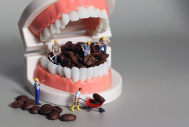 Minyatür insanlar kahve çekirdeklerini ağızlarıyla temizliyorlar. Diş sağlığı bozuk içecek konsepti.