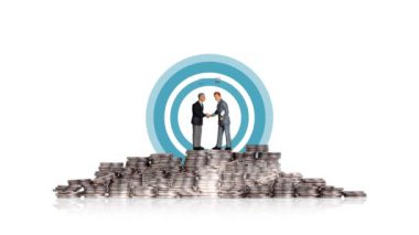 İki minyatür adam bozuk para yığınının üstünde el sıkışıyor. Bozuk para ve grafik yığınlarıyla işletme finans kavramı.