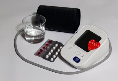 Measures blood pressure, monitors at all times, and detects diseases early. An electronic blood pressure gauge on a white background, a pill, and a glass of water. clipart