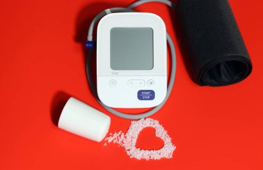 Electronic blood pressure gauge and electrocardiogram-shaped salt on a red background. Eating salt can increase high blood pressure and heart disease. clipart