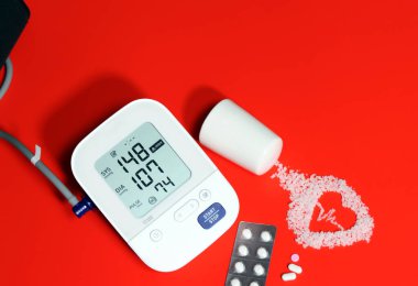 On a red background lies medicine, electrocardiogram-shaped salt, and an electronic blood pressure gauge. Eating salt can increase high blood pressure and heart disease. clipart