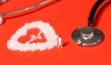 Obese people are more vulnerable to cardiovascular disease. Stethoscope on red background, salt in the shape of electrocardiogram, miniature people. clipart