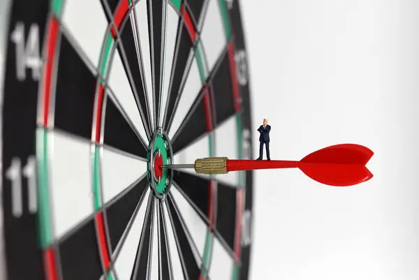 Business marketing success concept. A miniature businessman standing on a red arrow in the middle of a dart paper.