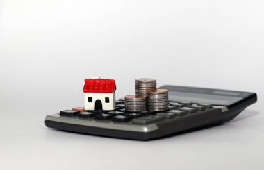 Hesap makinesine bir ev modeli ve bir yığın bozuk para yerleştiriliyor. İş yatırımı ve emlak vergisi kavramı.