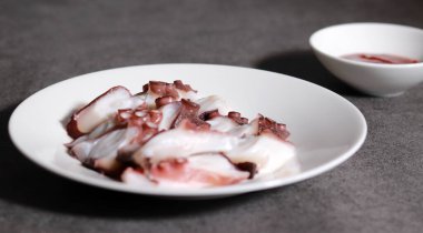 İnce dilimlenmiş ahtapot ve beyaz tabakta kırmızı biber ezmesi. Taze deniz ürünleri..