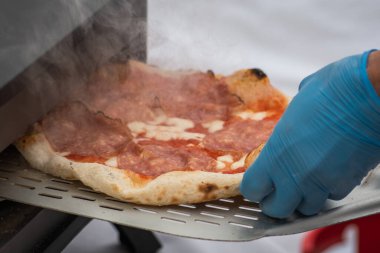 Plastik eldiven ile pişirme veya pişirme domates soslu sıcak pizza, mozzarella ve elektrikli ya da gaz fırınında kürekle salam eti, dumanla yakın çekim