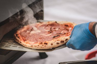 Plastik eldiven ile pişirme veya pişirme domates soslu sıcak pizza, mozzarella ve elektrikli ya da gaz fırınında kürekle salam eti, dumanla yakın çekim