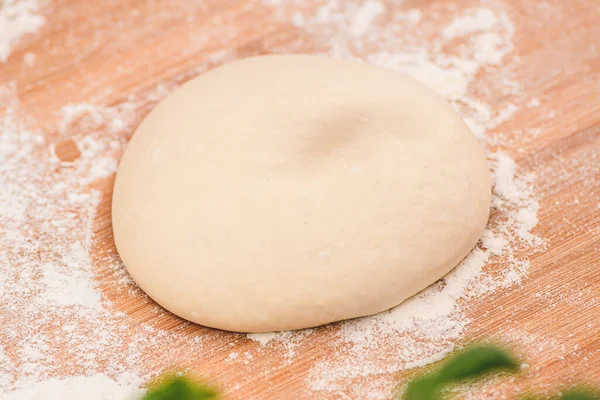 stock image Dough for pizza on a wooden board with white flour and ingredients around ready for preparation, close up