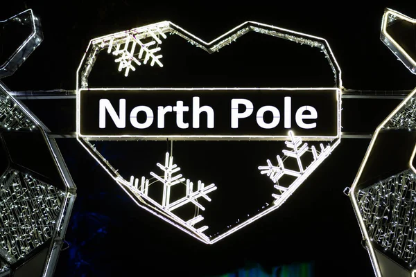 North Pole written in a heart with snowflakes made with the glowing lights, with northern lights and black background