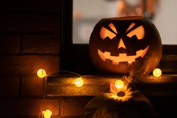 Spooky Halloween pumpkin, Jack O Lantern with pumpkins lights hanging from a window during a party