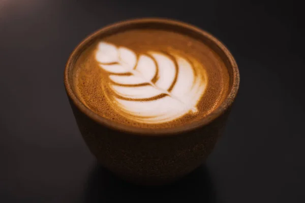 Close up Cappuccino in a ceramic cup with flower or leaves drawn on the foam, black background, view from above