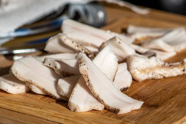 Pieces of lard or bacon, sliced thinly for consumption, on a wooden cutting board in a street food market, close up