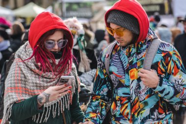 Trakai, Vilnius, Lithuania - February 19 2022: Beautiful young couple with colourful clothes, glasses, tattoos and smartphone traveling and walking in the street 