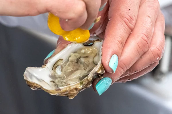 stock image Wet hands of a girl with painted nails squeezing a lemon on an oyster before eating, close up