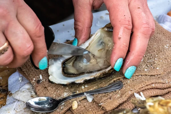 stock image Wet hands of a girl with painted nails opening an oyster with a small knife in a fish shop or street food market