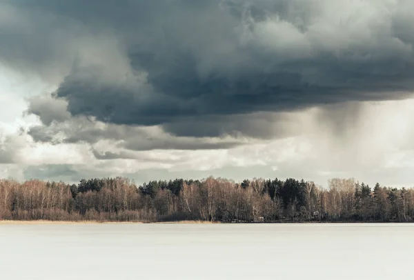 凍った湖 水平線の森 遠くに灰色の雲と雪が降る劇的な空 嵐が来る — ストック写真