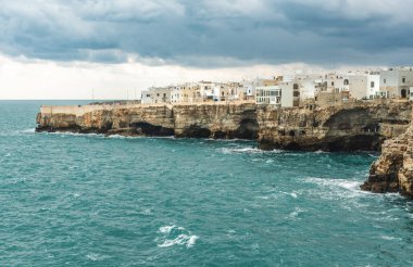 Polignano a Mare, Bari, İtalya. Kayalık kayalıkların üzerine inşa edilmiş eski bir kasaba. Geleneksel evleri, dramatik bulutlu gökyüzü ve güzel Akdeniz manzaralı seyahat konsepti