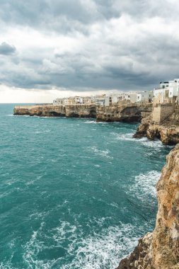 Polignano a Mare, Bari, İtalya. Kayalık kayalıkların üzerine inşa edilmiş eski bir kasaba. Geleneksel evleri, dramatik bulutlu gökyüzü ve güzel Akdeniz manzaralı seyahat konsepti