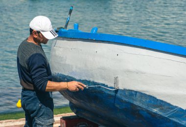 Bari, Puglia, İtalya - 8 Nisan 2023: Puglia İtalya 'nın Bari limanındaki eski bir ahşap balıkçı teknesini tamir eden ve boyayan balıkçı