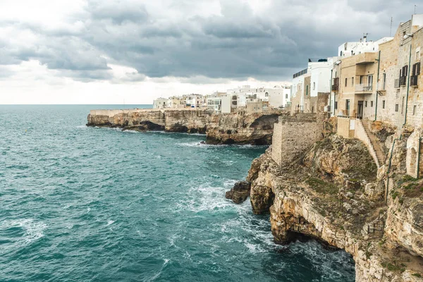 Polignano a Mare, Bari, İtalya. Kayalık kayalıkların üzerine inşa edilmiş eski bir kasaba. Geleneksel evleri, dramatik bulutlu gökyüzü ve güzel Akdeniz manzaralı seyahat konsepti